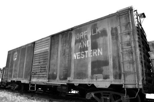 A weathered Norfolk and Western train car, shown in black and white, parked on a railway track.