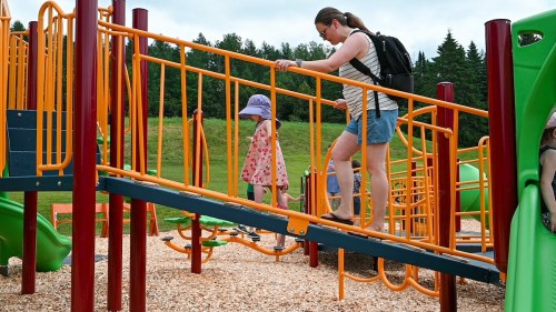 A woman and a child navigate a colorful playground structure with climbing elements and slides.