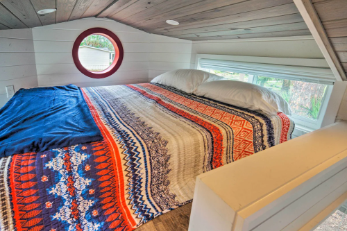 Cozy loft bedroom with a round window, featuring a colorful patterned blanket and two pillows on a bed.