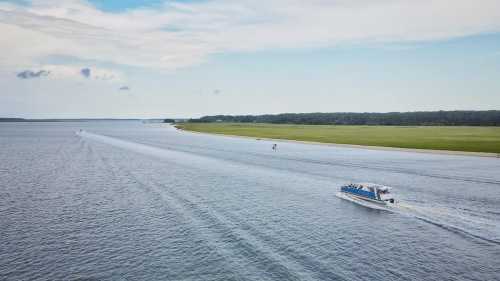 Aerial view of boats on a calm waterway, with green land and a cloudy sky in the background.