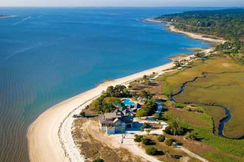 Aerial view of a coastal property with a sandy beach, blue water, and lush greenery along the shoreline.