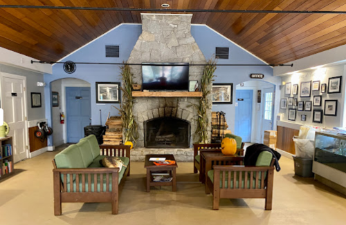 Cozy lobby with a stone fireplace, wooden furniture, and a TV, featuring warm lighting and decorative photos on the walls.