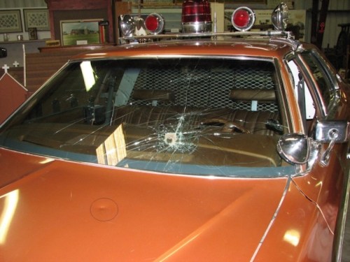 An orange vintage police car with a cracked windshield and a light bar on top, parked indoors.