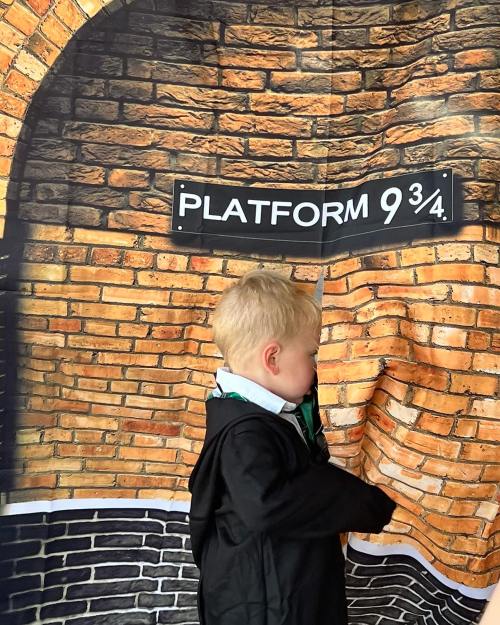 A child in a black coat stands beside a brick wall backdrop labeled "Platform 9¾."