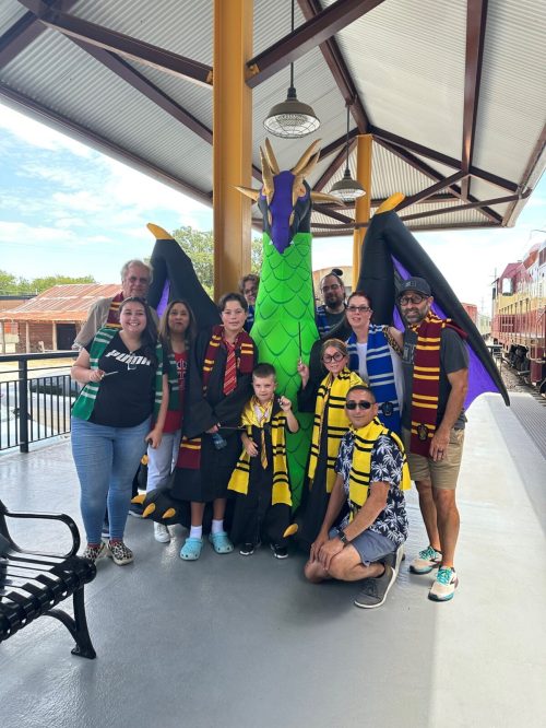 A group of people in scarves poses with a large dragon statue at a train station.