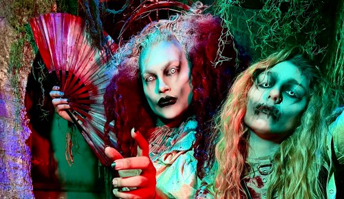 Two spooky figures with dramatic makeup and eerie expressions, surrounded by colorful lighting and eerie decorations.