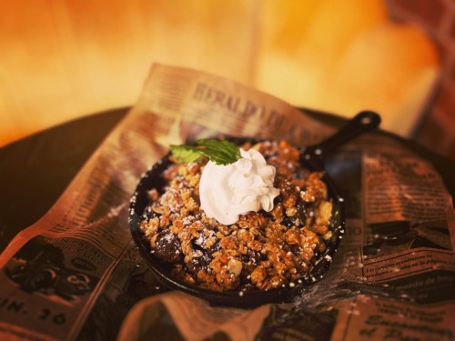 A warm dessert in a cast-iron skillet topped with whipped cream and mint, served on a bed of newspaper.