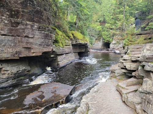 A serene river flows through rocky cliffs, surrounded by lush greenery and trees in a peaceful natural setting.