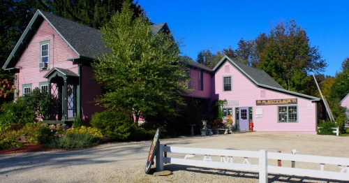 A charming pink building with a sign reading "R.S. Butler's," surrounded by greenery and a gravel pathway.