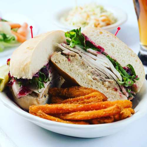 A sandwich with turkey, lettuce, and cranberry sauce, served with sweet potato fries on the side.