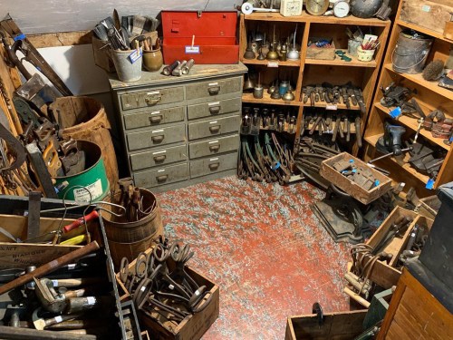 A cluttered workshop filled with various tools, cabinets, and wooden boxes, showcasing a variety of hand tools and equipment.