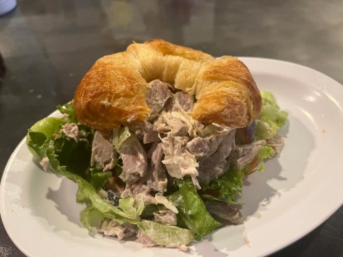 A croissant sandwich filled with chicken salad and lettuce, served on a white plate.