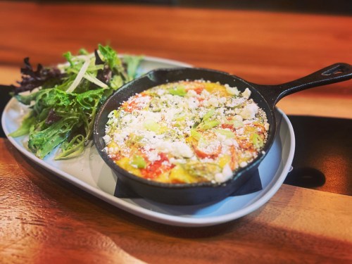 A colorful frittata in a cast iron skillet, served with a side of mixed greens on a wooden table.