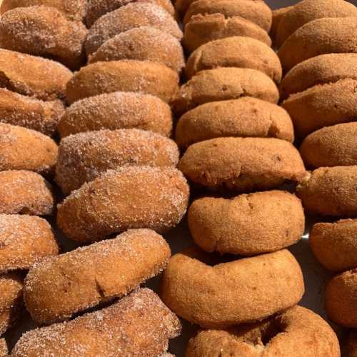 A close-up of freshly baked donuts arranged in rows, some coated in sugar and others plain.