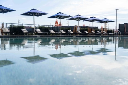 A serene pool scene with lounge chairs and umbrellas, reflecting the sky and surrounding greenery.