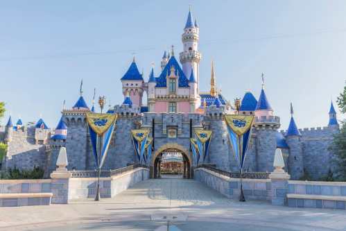 A colorful castle with blue spires and banners, set against a clear blue sky, resembling a fairytale scene.