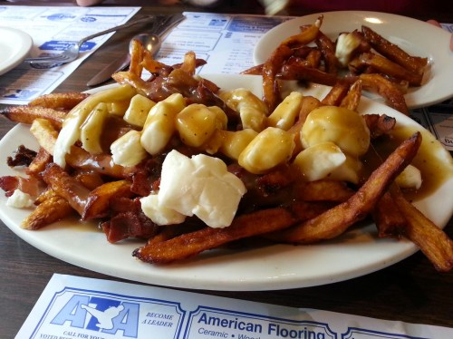A plate of poutine topped with cheese curds and gravy, served with crispy fries and bits of bacon.