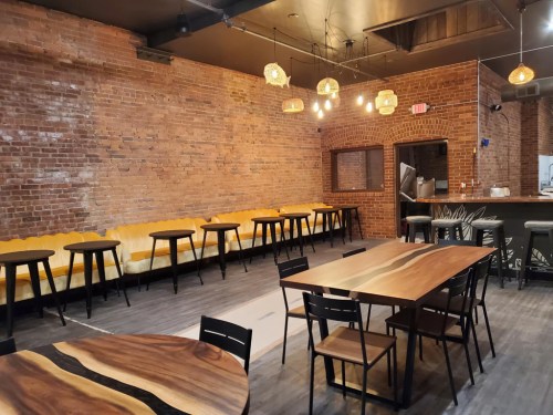 Interior of a restaurant featuring exposed brick walls, wooden tables, and a cozy seating area with yellow couches.