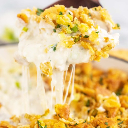 A spoon lifting creamy, cheesy casserole topped with crispy golden crumbs and green onions.