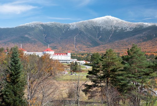 A scenic view of a mountain with autumn foliage, featuring a large hotel in the foreground and a clear blue sky.