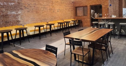 Interior of a restaurant featuring brick walls, wooden tables, and a yellow couch along with high-top seating.