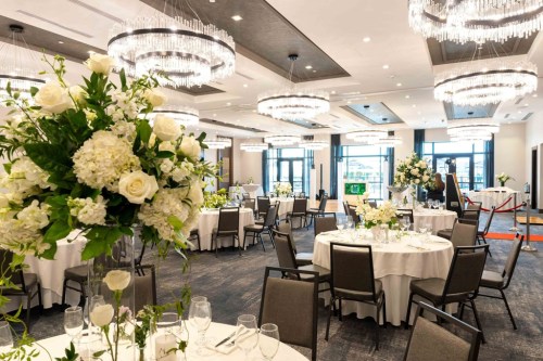 Elegant banquet hall with round tables, white floral centerpieces, and chandeliers, ready for an event.