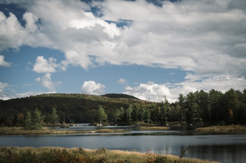 A serene lake surrounded by trees and rolling hills under a partly cloudy sky.