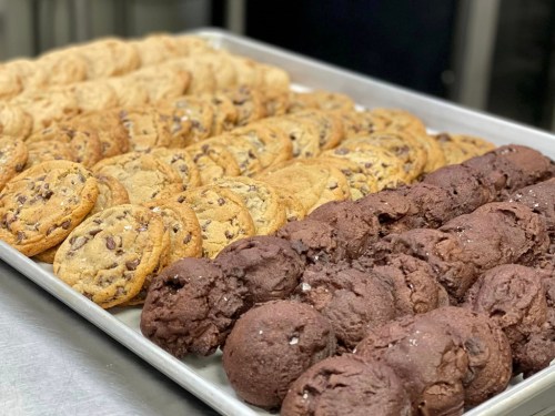 A tray of freshly baked cookies, featuring chocolate chip and chocolate varieties, arranged neatly in rows.