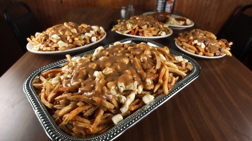 A large platter of fries topped with gravy and cheese curds, surrounded by smaller plates of similar dishes on a wooden table.