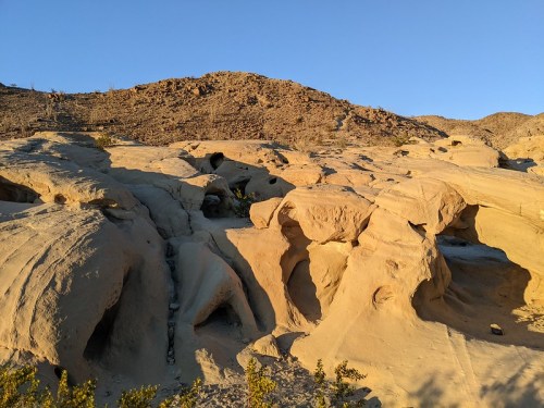 A rocky desert landscape with textured sandstone formations under a clear blue sky.