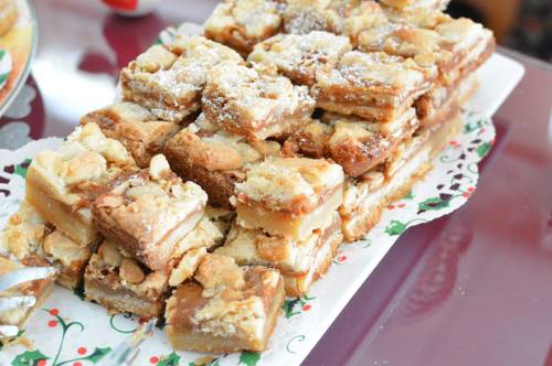 A plate of stacked dessert bars dusted with powdered sugar, featuring a crumbly topping and a caramel-like filling.