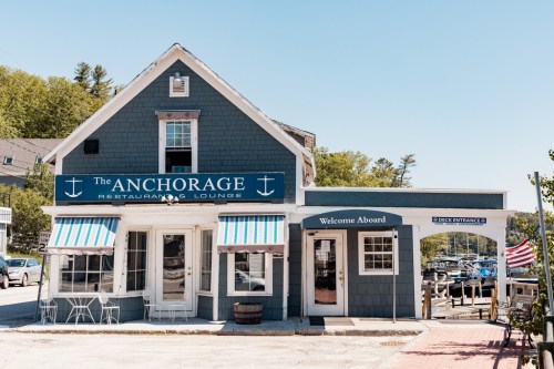 A charming blue restaurant with white trim, featuring striped awnings and a sign that reads "The Anchorage."