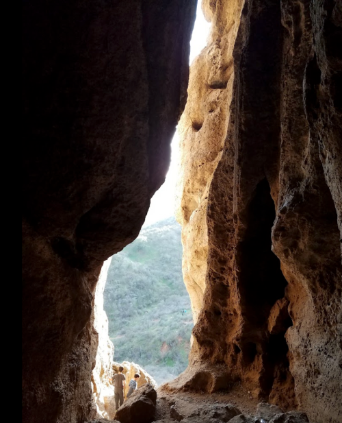 A person stands at the entrance of a cave, with sunlight streaming in and illuminating the rocky interior.