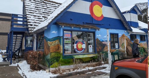 Colorful building with a Colorado flag mural, snowy surroundings, and a "OPEN" sign in the window.