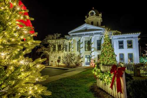 A beautifully lit historic building adorned with Christmas decorations, surrounded by festive trees and lights at night.