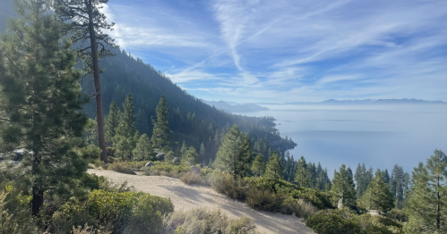 Scenic view of a calm lake surrounded by mountains and lush green trees under a clear blue sky.
