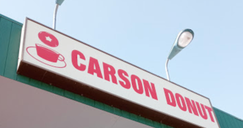 Sign for "Carson Donut" featuring a coffee cup and donut graphic, with streetlights in the background.