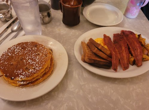 A plate of fluffy pancakes dusted with powdered sugar, and another plate with scrambled eggs, bacon, and toast.