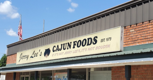 Sign for Jerry Lee's Cajun Foods, established in 1979, with an American flag in the background.