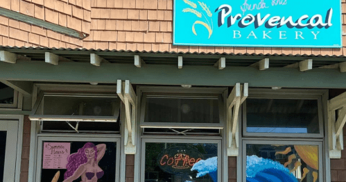 A bakery storefront with a colorful sign and artistic window displays featuring a woman and ocean waves.