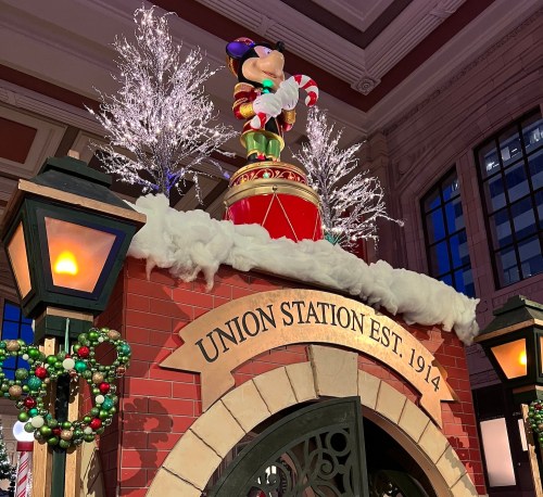 A festive display at Union Station features a large Mickey Mouse on a drum, surrounded by snowy decor and holiday lights.