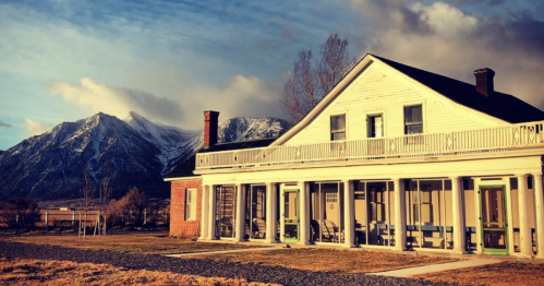 Historic building with a porch, set against snow-capped mountains and a dramatic sky.