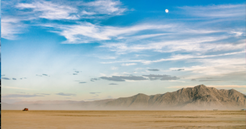 A vast desert landscape with mountains in the background, a clear blue sky, and a bright moon overhead.
