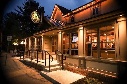 A warmly lit restaurant exterior at dusk, featuring a sign that reads "The Perk" and inviting entrance steps.
