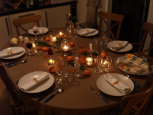 A beautifully set dining table with candles, plates, and seasonal decorations, ready for a festive meal.