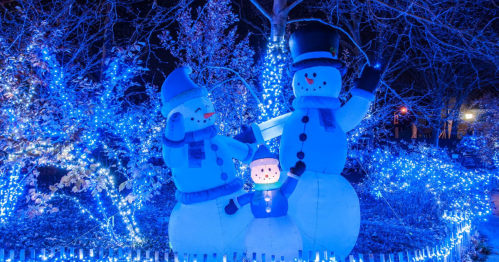 Two large inflatable snowmen with blue lights, surrounded by glowing trees, create a festive winter scene at night.