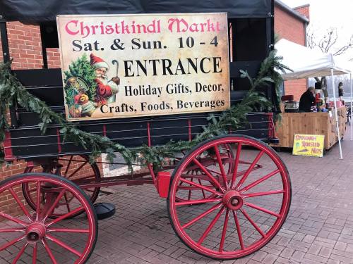 Sign for Christkindl Market with Santa, announcing entrance hours and featuring holiday gifts, decor, and food.