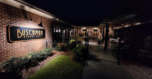 Exterior view of Buschman Street Cafe at night, featuring brick walls, outdoor seating, and warm lighting.