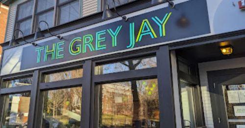 Sign for "The Grey Jay" restaurant with neon green letters on a building exterior.