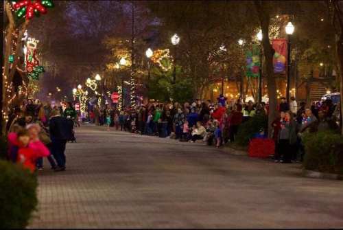 A festive street lined with people enjoying holiday lights and decorations, creating a cheerful atmosphere.